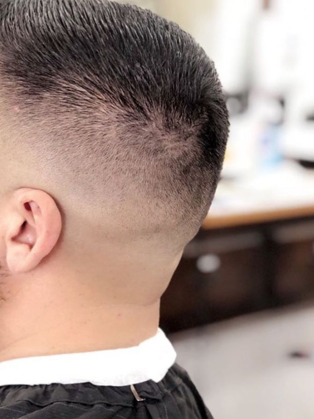 Side-back view of a man's mid skin fade with a short textured top, barber cape