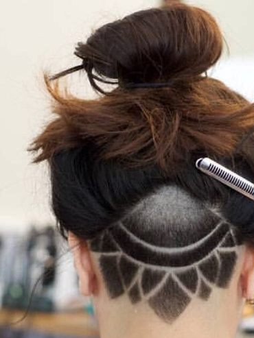 Back of a woman's head with a lotus pattern shaved into the undercut below a messy bun